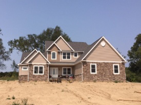 Multi-level brown house with brick and siding on lot without grass.