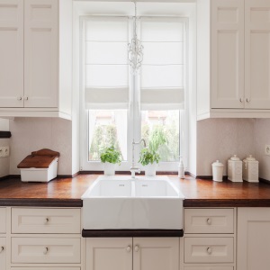 White apron sink beneath a window with white cabinets.